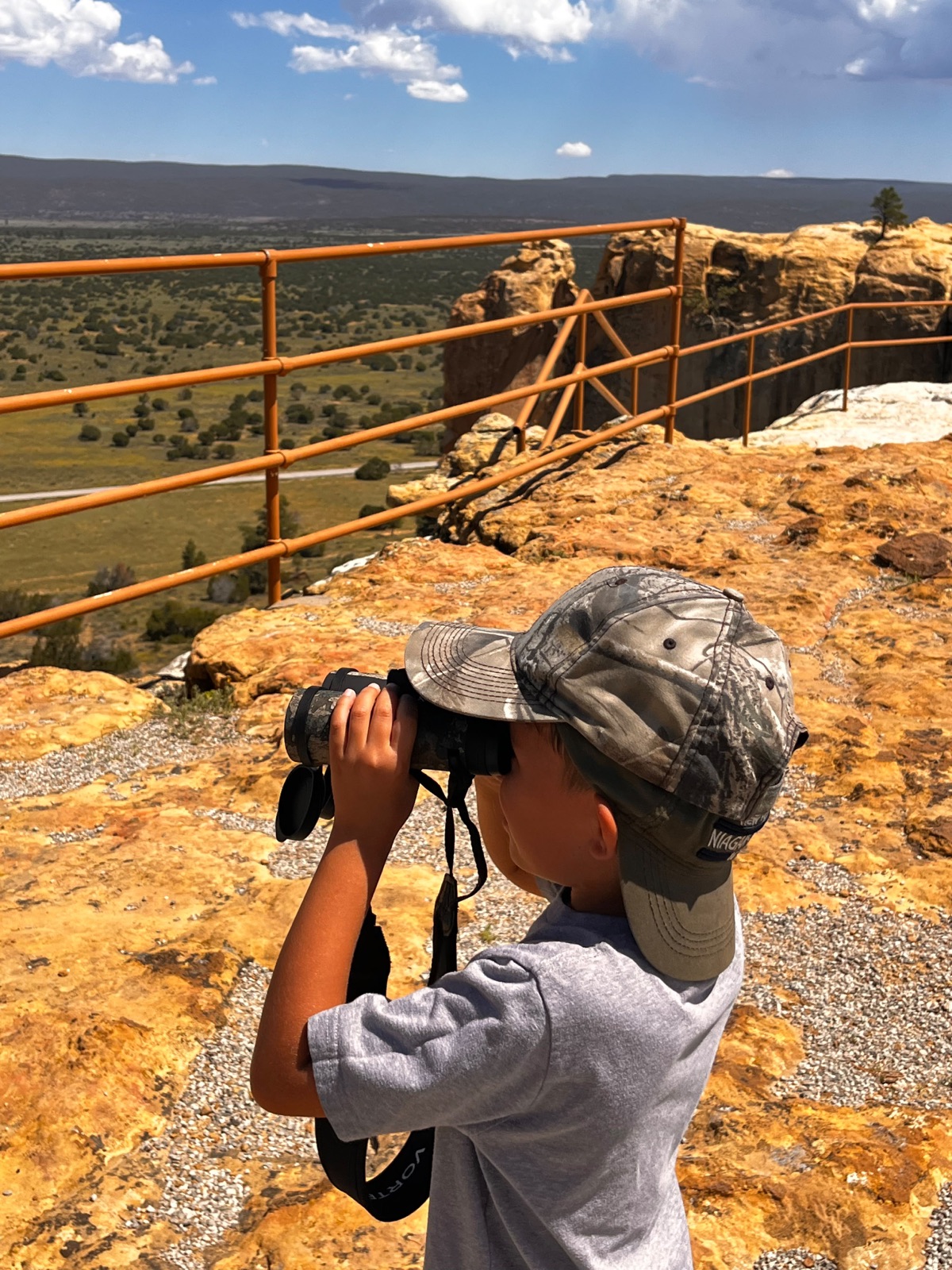 A boy looking out over the desert through binoculars from a cliff overlook